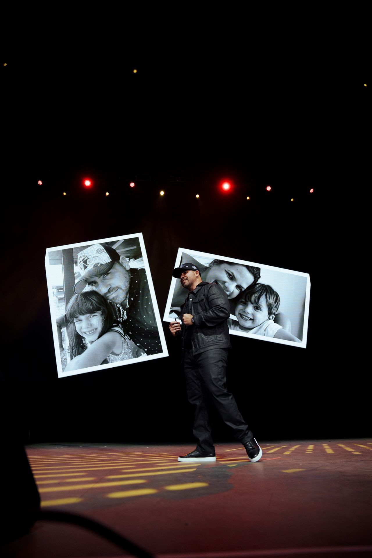 Man on stage with two large pictures of happy families, and red and yellow lights overhead.