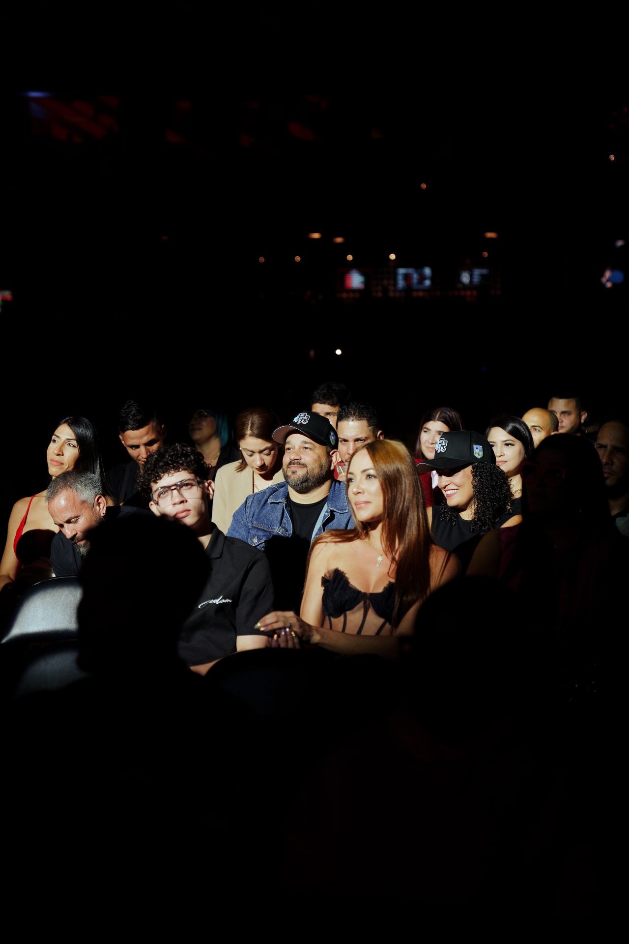 Audience sitting in a dimly lit venue, watching an event with focused expressions.