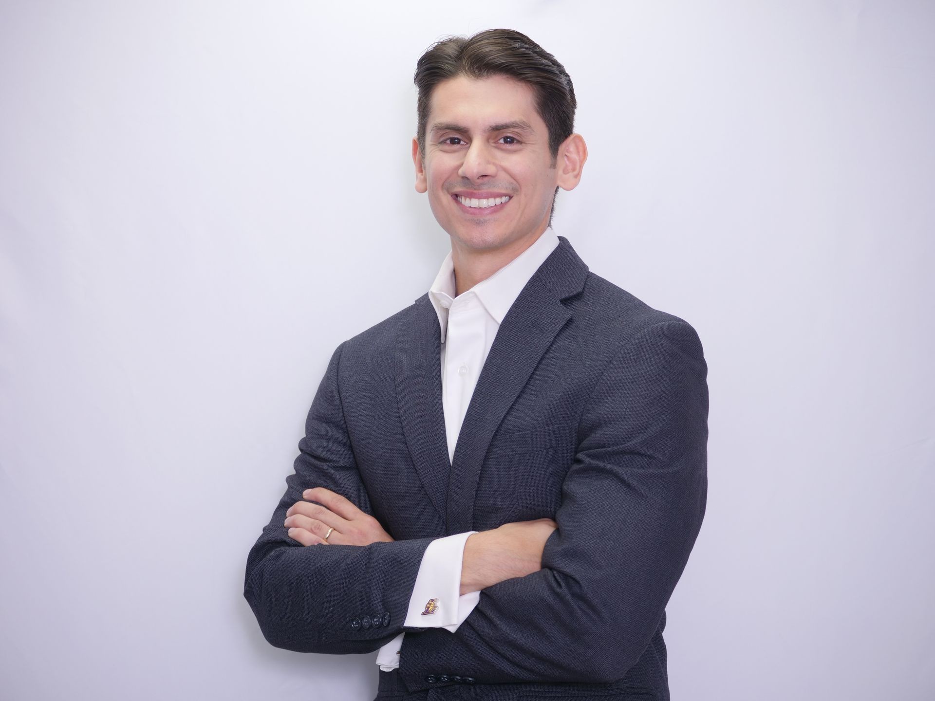 Smiling man in a dark suit with arms crossed, standing against a plain white background.