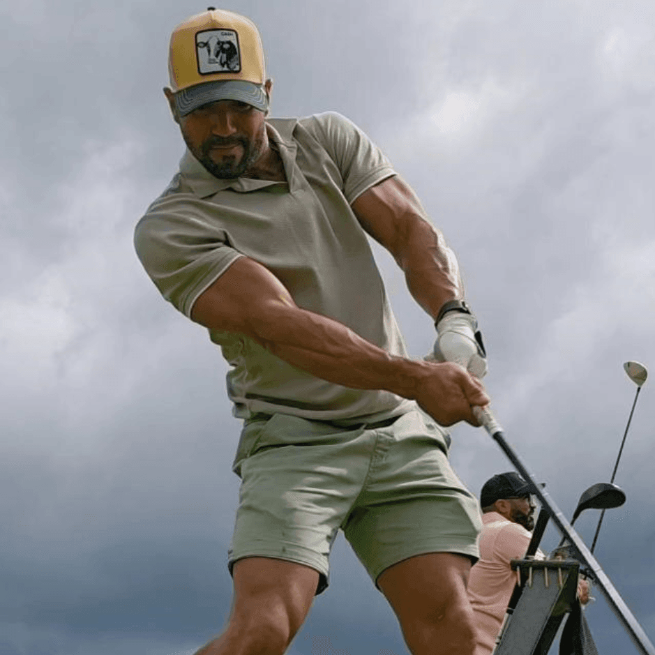 Man in a casual outfit practicing his golf swing outdoors, with cloudy skies in the background.